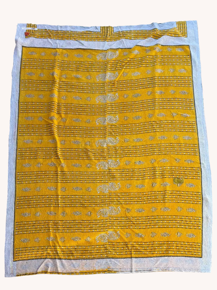 Yellow fabric with gold patterns on a white border, laid flat on a concrete surface.