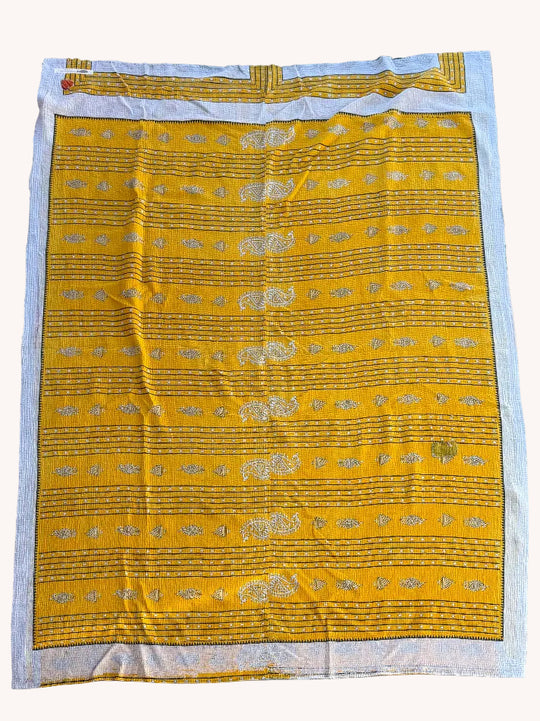 Yellow fabric with gold patterns on a white border, laid flat on a concrete surface.