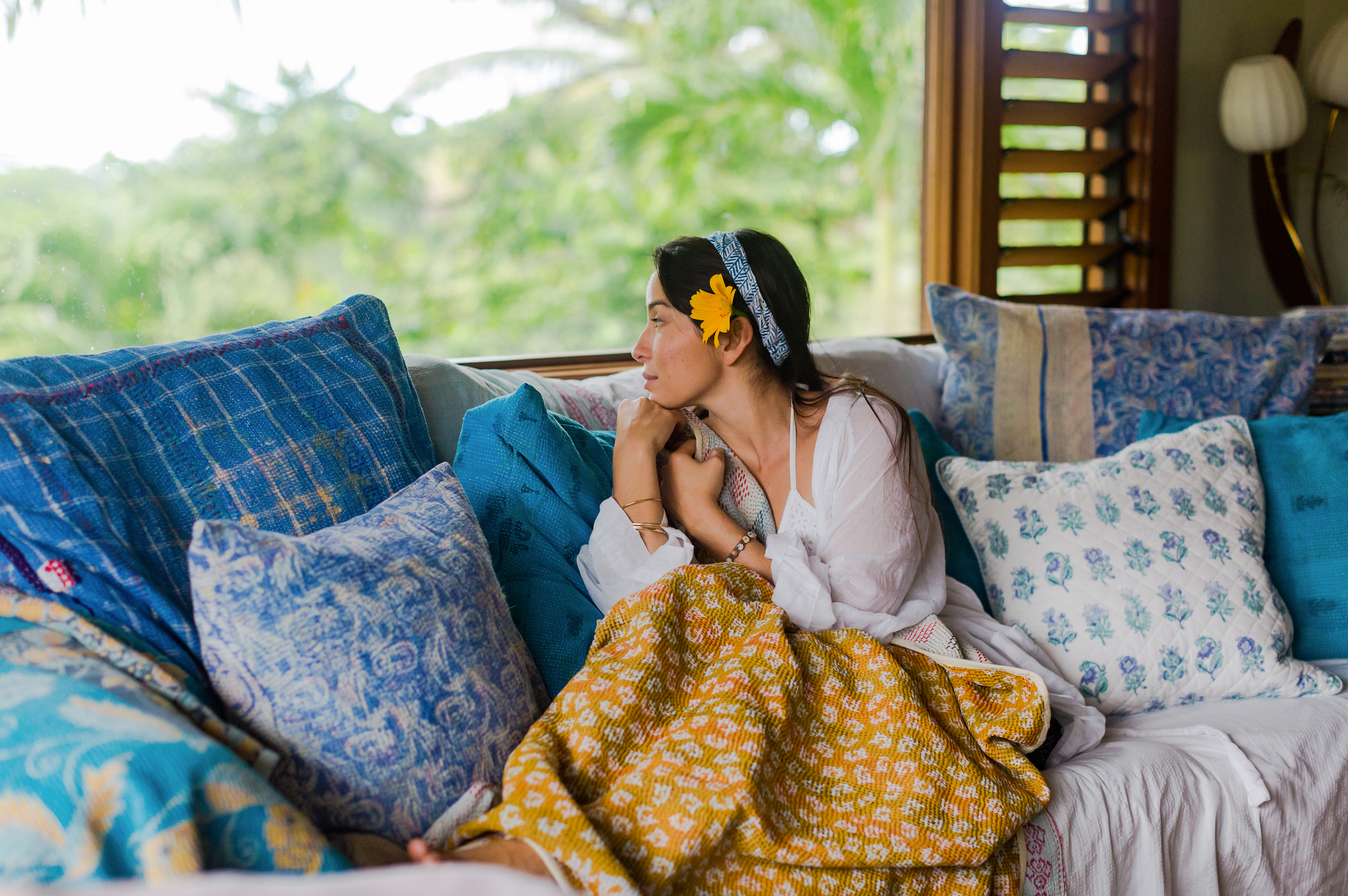 woman on a cozy daybed day dreaming surrounded by organic kantha pillows and quilts